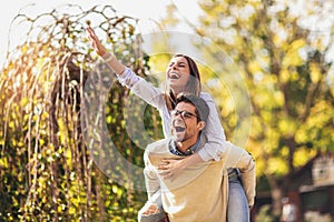 Couple having fun man giving piggyback to woman in park