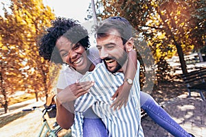 Couple having fun in park on autumn day. Handsome man giving piggy back to his girlfriend