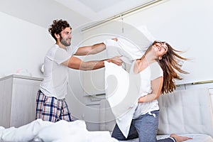 Couple having a fun while pillow fight. Young happy couple beat the pillows on the bed in a bedroom at home