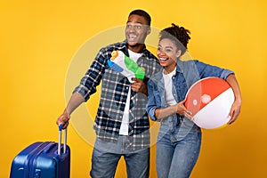 Couple Having Fun Posing With Suitcase And Toys, Yellow Background