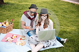 Couple having picnic and using laptop in park