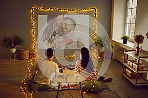 Couple having Valentine& x27;s date at home, using projector, watching movie or looking at photos