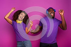 Couple with headset listen to music and dance with energy on violet background