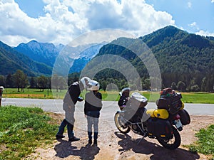 Couple in helmets are kissing. Motorcyclist adventure riders. Green meadow in Zgornje Jezersko, to Kamnik-Savinja Alps on a sunny