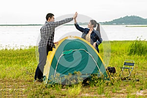 Couple helping installing tent camping outdoor near river and meadow.