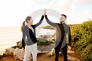 Couple high-fiving during sunset workout by the sea.