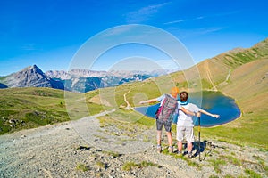 Couple of hiker on the mountain top looking at blue lake and mountain peaks. Summer adventures on the Alps. Wide angle view from a