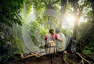 Couple hikers with backpacks enjoying view waterfall in rain for