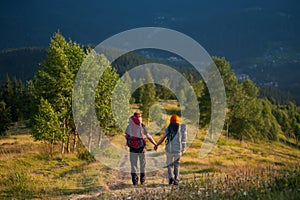 Couple hikers with backpacks holding hands, walking in the mountains