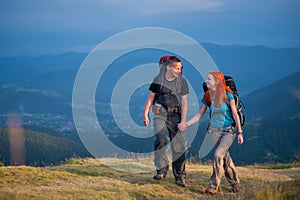 Couple hikers with backpacks holding hands, walking in the mountains