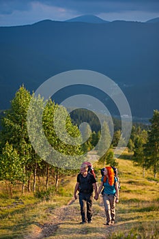Couple hikers with backpacks holding hands, walking in the mountains