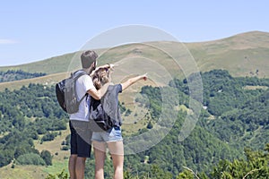 Couple of hikers with backpacks standing at viewpoint and enjoyi