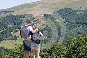 Couple of hikers with backpacks standing at viewpoint and enjoyi