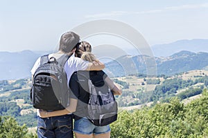 Couple of hikers with backpacks standing at viewpoint and enjoyi