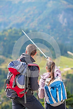 Couple of hikers showing the way with trekking poles up on the mountain peak