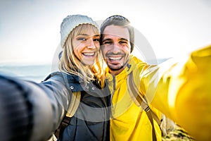 Couple of hikers taking a selfie climbing mountains - Man and woman with backpack smiling at camera - Bright filter