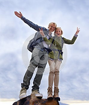 Couple, hiking and excited on mountain top for travel, success and achievement with peace sign on cloudy sky. Portrait