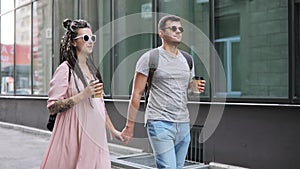 Couple of hipsters man and pregnant woman walking in city holding hands.