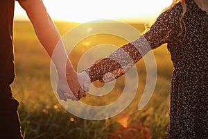 Couple hold hands in the autumn or summer park on sunset. Closeup of loving couple holding hands while walking