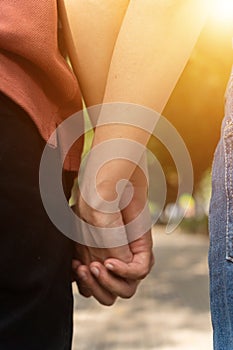 Couple hold hands in the autumn or summer park on sunset. Closeup of loving couple holding hands while walking