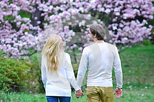 Couple hold hands in spring park, back view. Woman and man date in blossoming garden. Spring, nature awakening, beauty