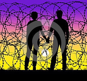 A couple hold hands and watch the sunset through a razor wire fence at the USA and Mexico border photo