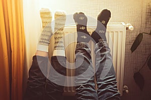 Couple hold legs up heating feet in cold home indoors on radiator in winter with cozy winter stylish woolen socks on. Valentines
