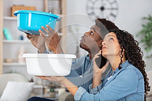 couple holding bowls under leaking ceiling and making phonecall