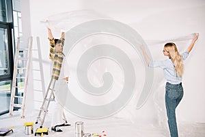 Couple holding cellophane while preparing for wall painting