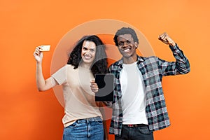 Couple Holding Credit Card and Tablet on Orange Background