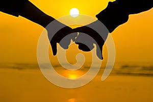 Couple holding each other hands using little pinky finger in background of sunrise at the beach