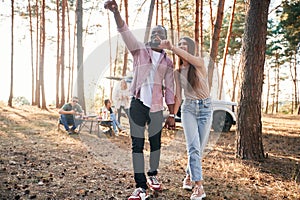 Couple are holding each other by the hands, walking. Group of friends are together in the forest