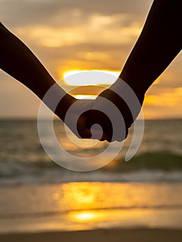 Couple holding hands on beautiful sunset background at the beach