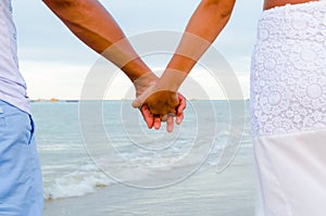 Couple holding hands having the sea as a background. View of the arms in the center and part of the bodies in the sides.