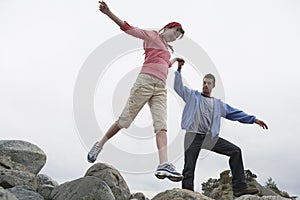 Couple Holding Hands And Jumping On Rocks