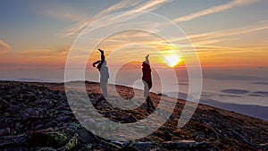 A couple holding hands and jumping on top of Babia Gora, Poland, with the panoramic view on sun rising above the horizon