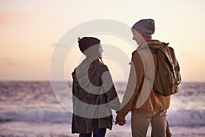 Couple, holding hands and love at sunset by beach, ocean waves and peace for romance in relationship. People, back and