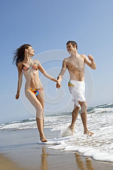 Couple Holding Hands While Running In Surf At Beach