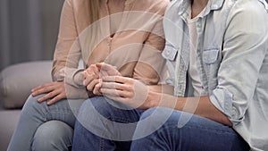 Couple holding hands, sitting in waiting hall hospital, fertility consultation