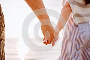 Couple holding hands at sunset on beach. Romantic man and woman enjoying sunset, romance and love by the sea. Couple on summer