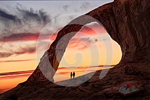 Couple holding hands under natural sandstone arch by the tent.