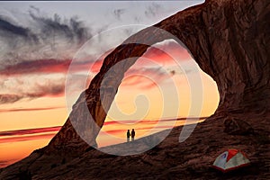 Couple holding hands under natural sandstone arch by the tent.