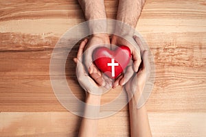 Couple holding heart with cross symbol on background, top view. Christian religion