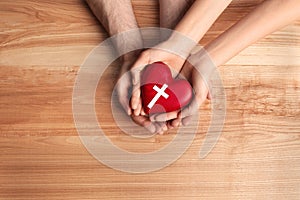 Couple holding heart with cross symbol on background, top view. Christian religion