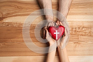 Couple holding heart with cross symbol on background, top view with space for text. Christian religion