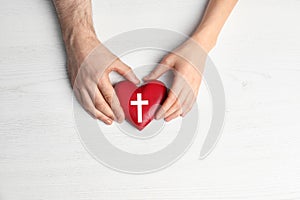 Couple holding heart with cross symbol on wooden background, top view. Christian religion