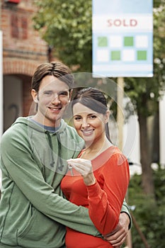 Couple Holding Key In Front Of New Home With Sold Sign