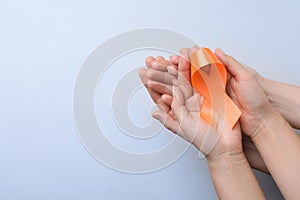 Couple holding orange ribbon on light grey background, top view with space for text. Multiple sclerosis awareness