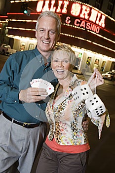 Couple Holding Playing Cards And Dices Against Casino