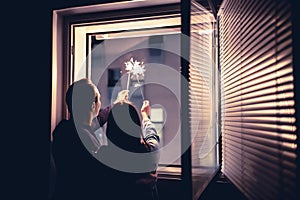 Couple holding sparklers out of the window at night. New year`s eve celebration, anniversary, party or date at home.